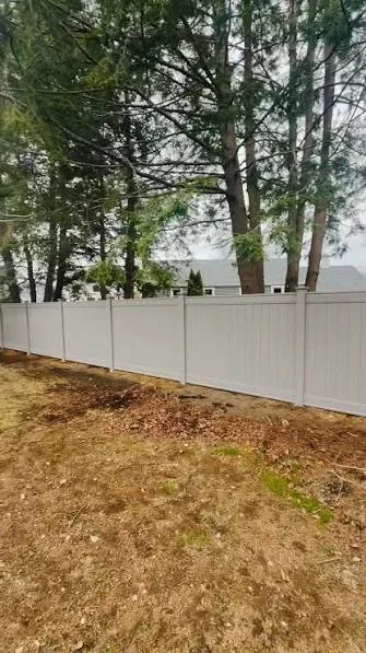 White vinyl privacy fence panels installed along tree line with mulch base