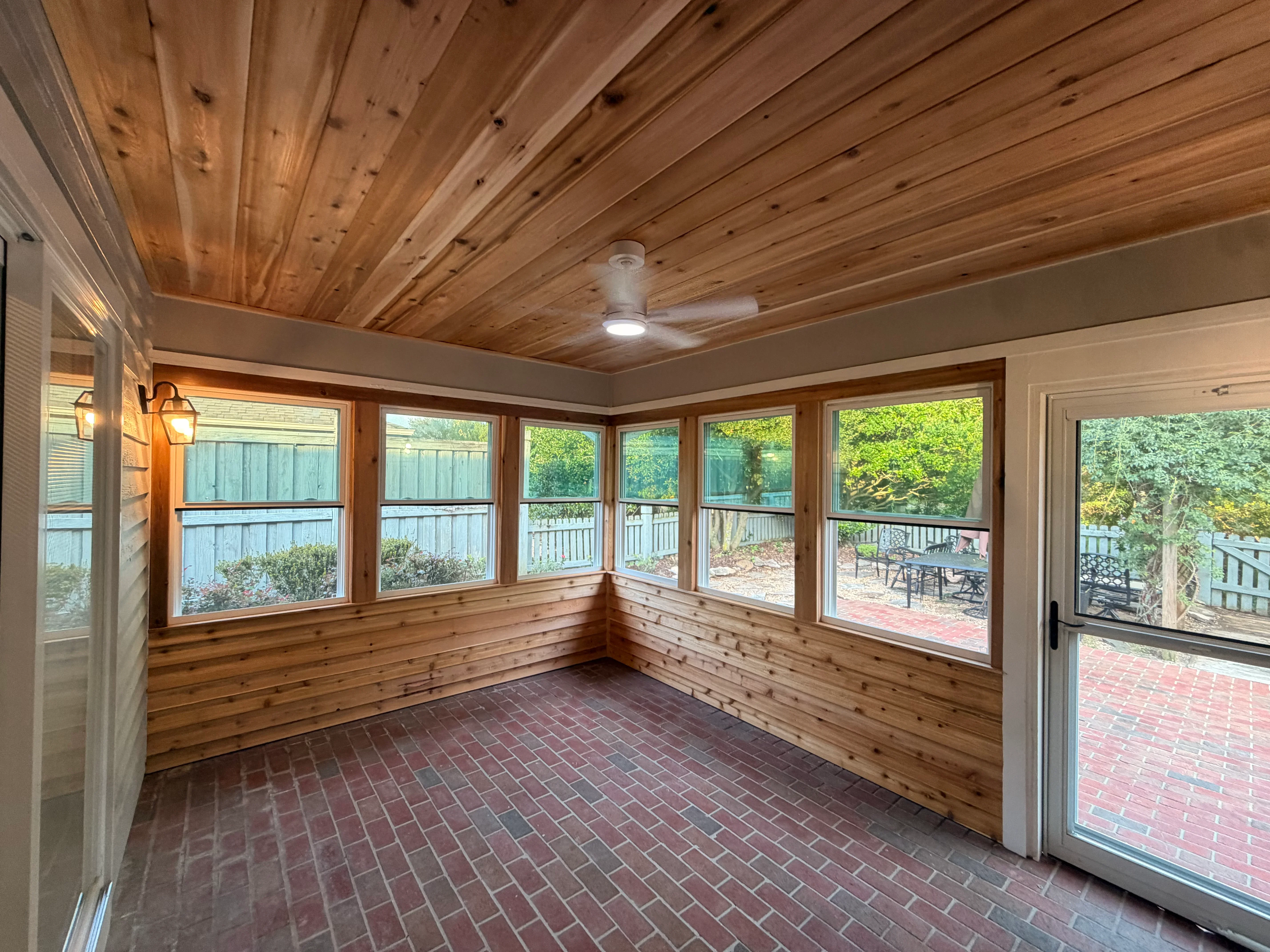 Cedar sunroom with wood ceiling and wainscoting, multiple windows, brick floor, and glass door