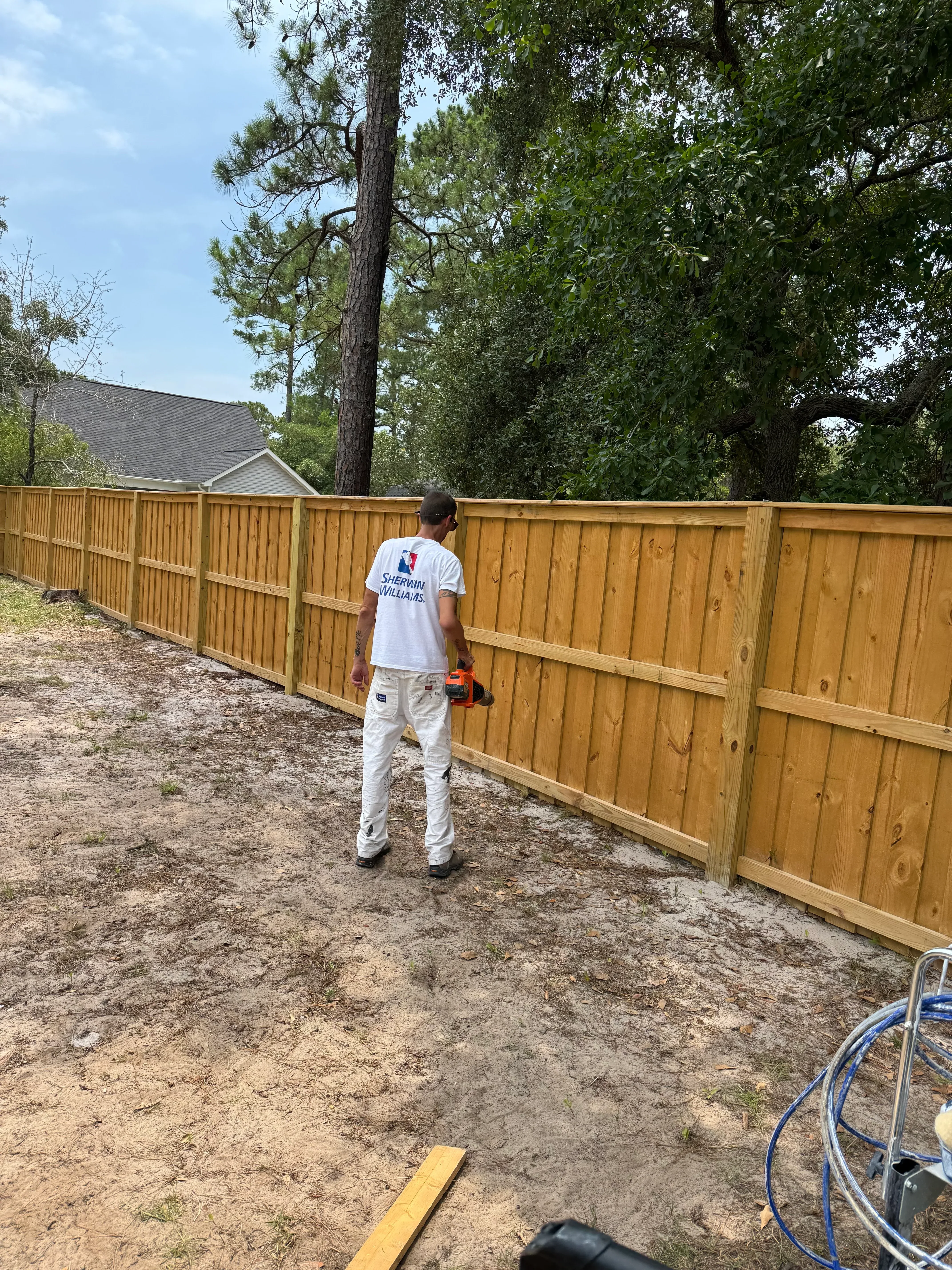Painter staining a new wood privacy fence in a backyard