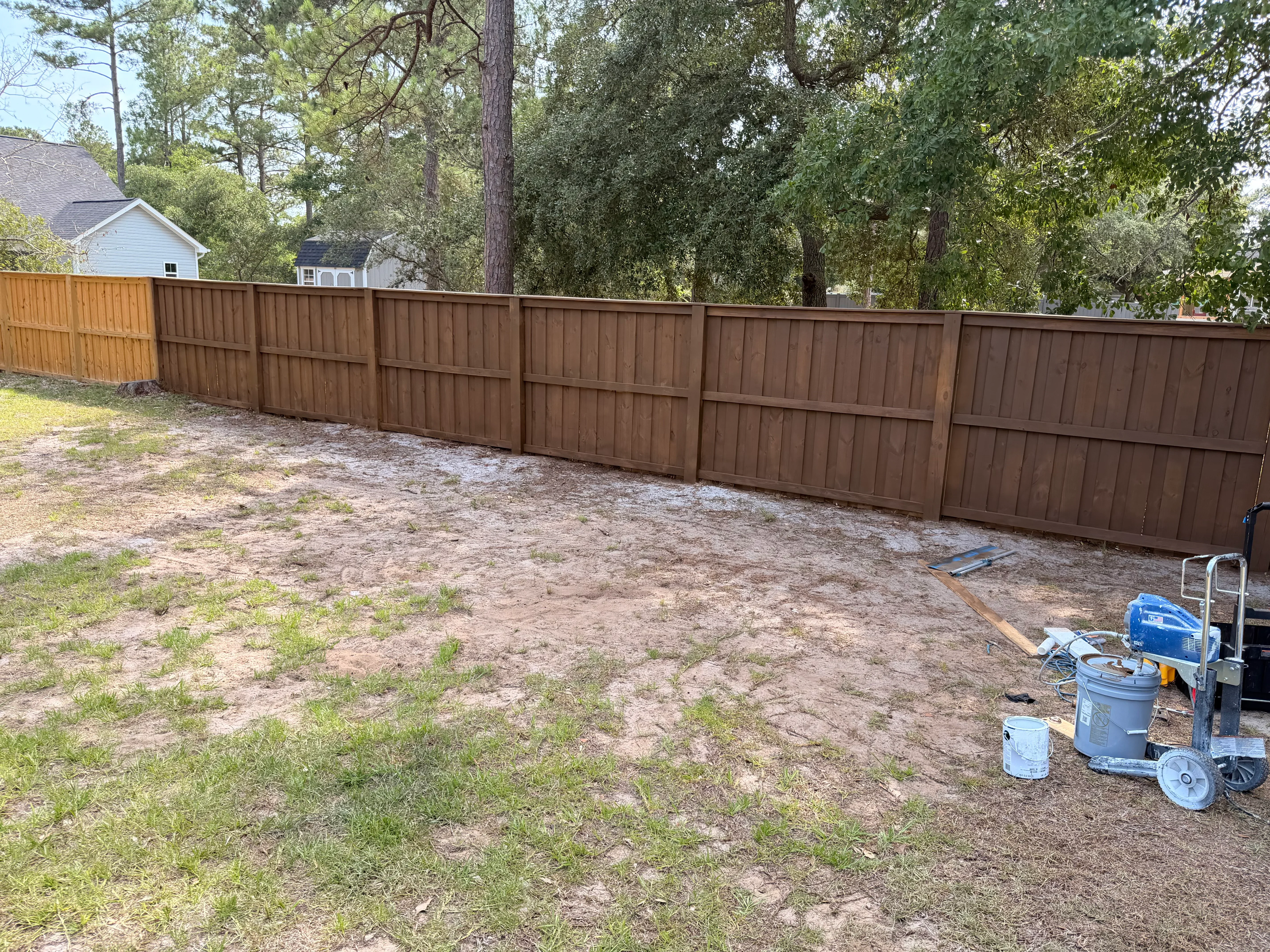 Brown vertical board privacy fence installation in residential backyard with mature trees