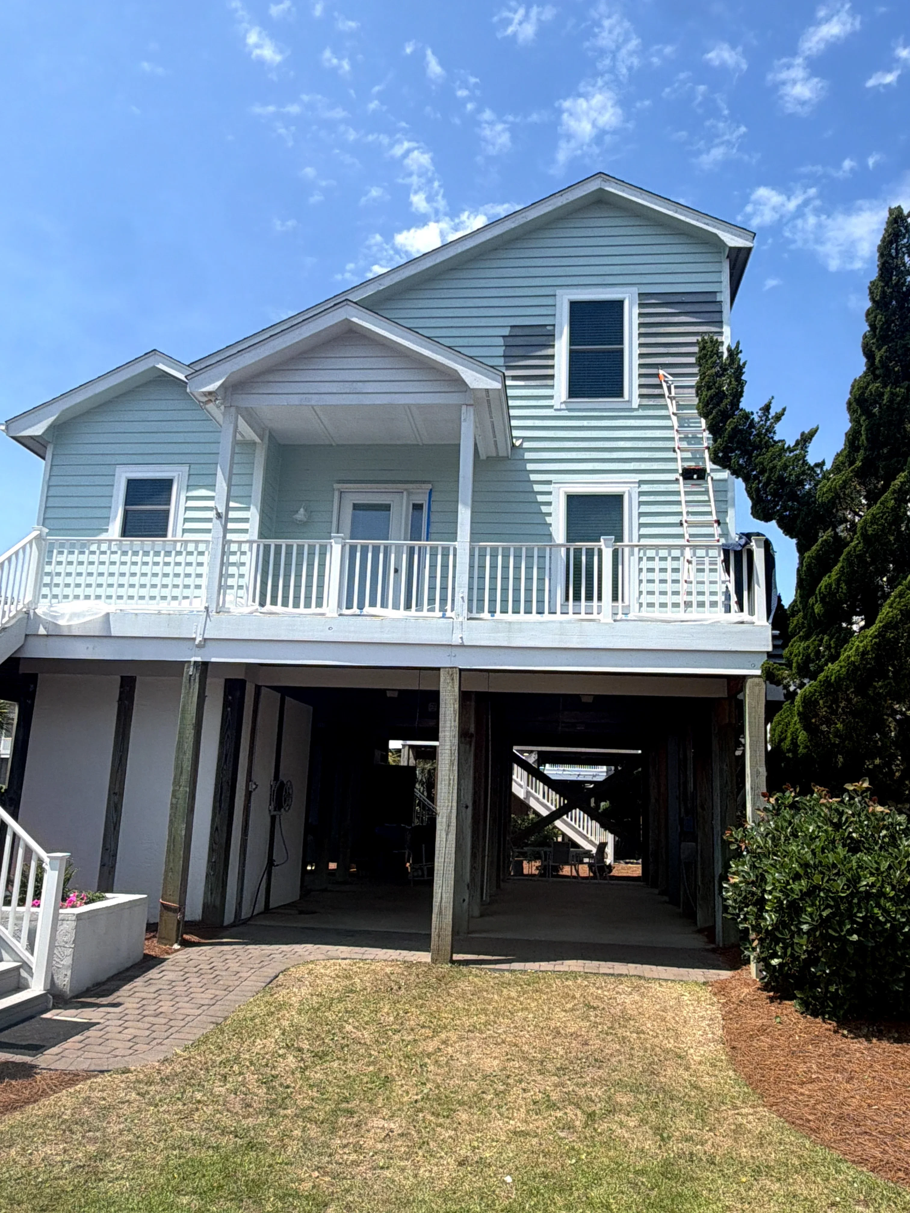 Elevated composite deck with white railings and stairs under raised coastal home